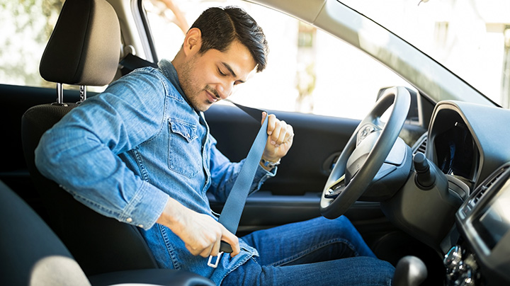 Young latin man sitting on car seat fastening seat belt