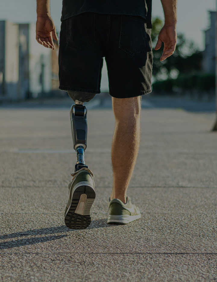 a cropped image of the back of a man with a prosthetic leg walking down a sidewalk