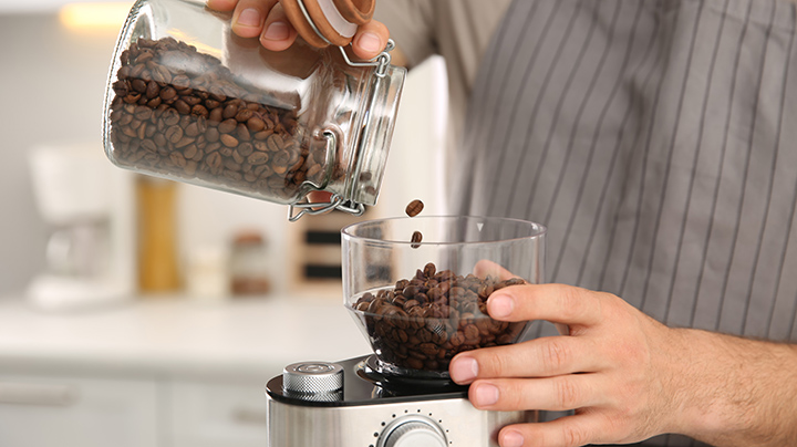 Man using electric coffee grinder in kitchen, closeup