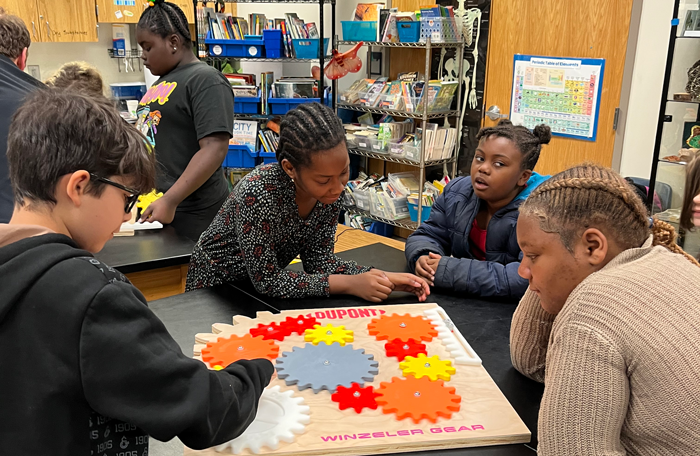 A group of students interacting collaboratively with a wooden board with gears