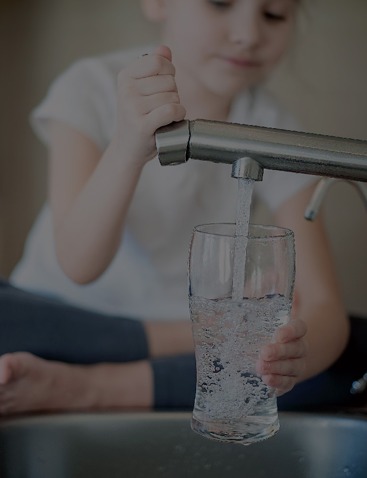 A child pours clean water from the faucet into a clear glass cup