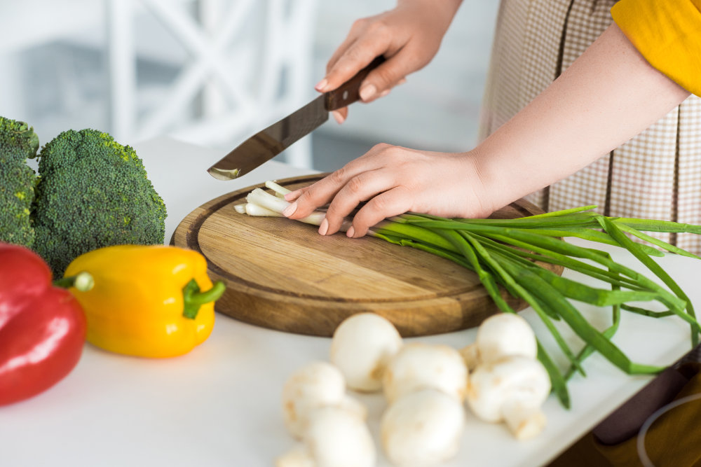 cropped image of woman cutting green onion on cutting board