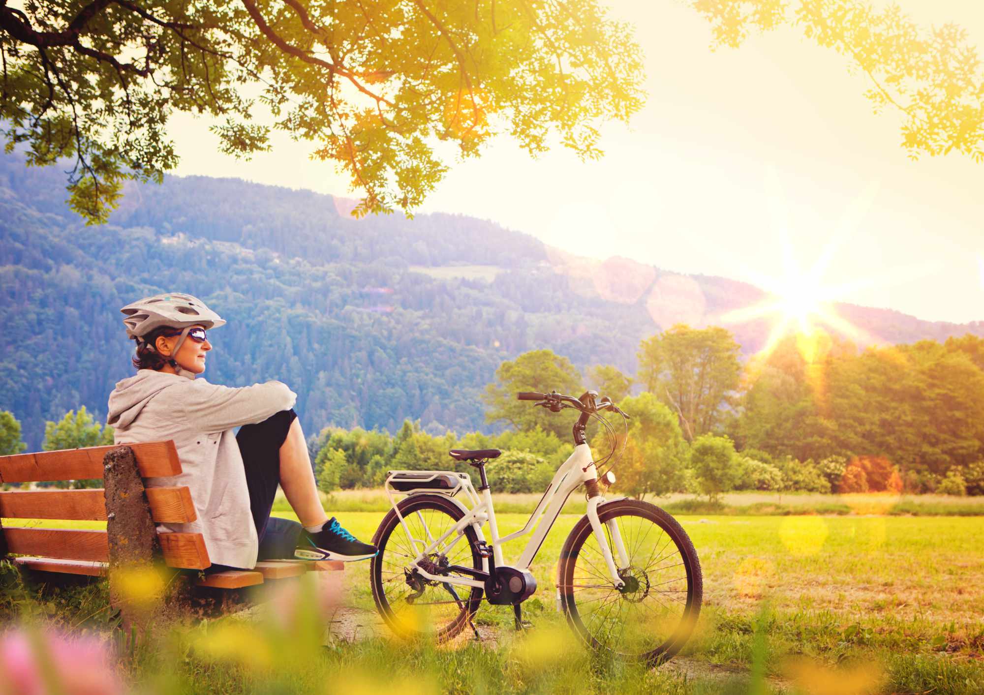 a woman relaxing on a bench next to her e-bike in a lush green park during sunset