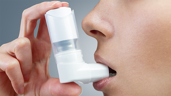 A zoomed in image of a woman managing respiratory symptoms with inhaler