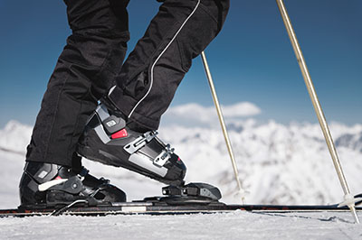 Close-up of the athlete's skier's foot in ski boots rises into the skis against the background of the snow-capped Caucasus mountains on a sunny day. Winter sports concept.